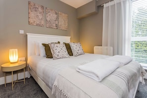 Ein ordentlich eingerichtetes Schlafzimmer mit einem Bett, einer Nachttischlampe und floralen Wandbildern.