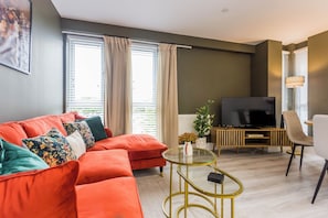Ein modernes Wohnzimmer mit einem roten Sofa, einem Glastisch, einem Flachbildfernseher und einem Essbereich mit einem Stuhl und Tisch.