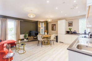 A modern living room with a red sofa, a dining table with chairs, a TV, and a kitchen area with a sink and cabinets. - The Autumn Ember at Parsons House (Washington)