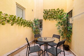 A small outdoor patio with a round table and four chairs, surrounded by potted plants and a yellow wall. - Cruz Verde 10 Suites Malaga (Malaga)