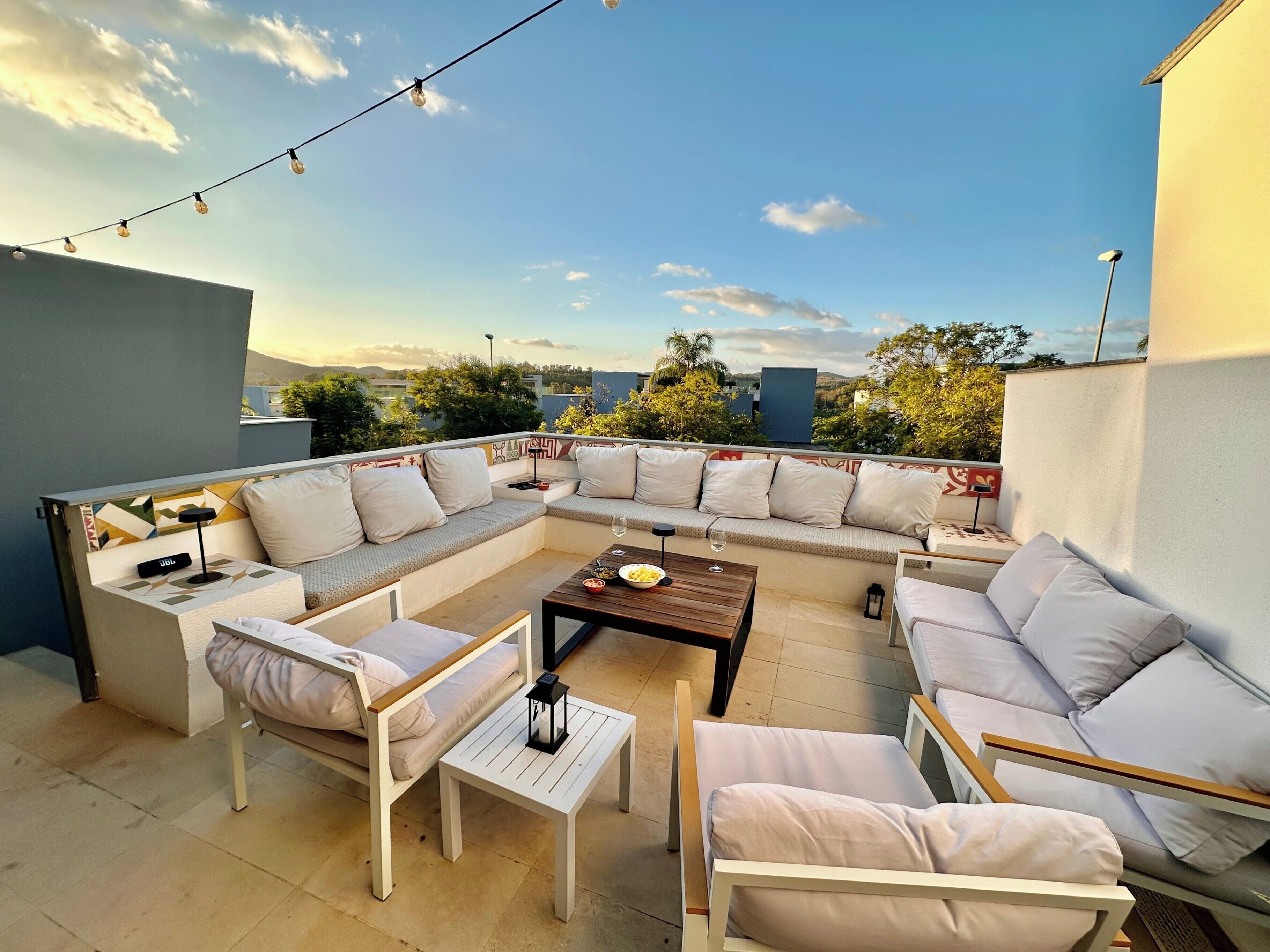 A rooftop patio with a sectional sofa, a small table, and string lights.