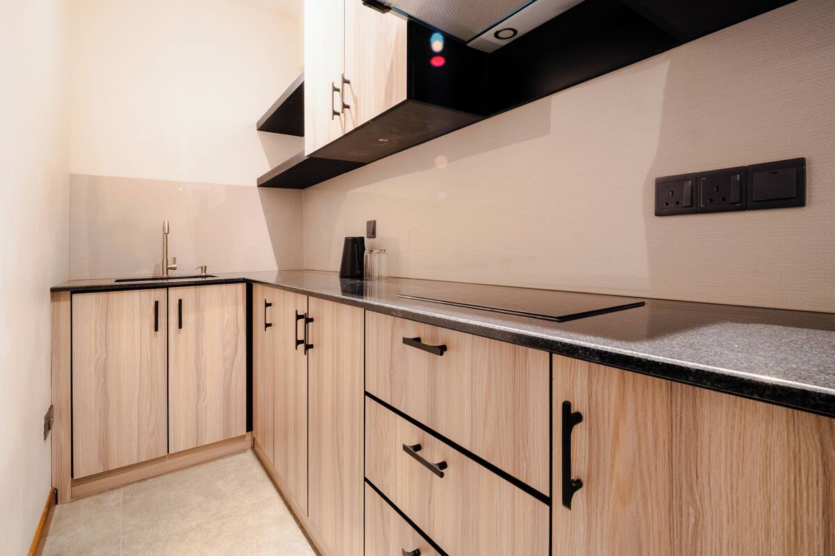 A kitchen with light wood cabinets, black handles, a black countertop, and a stainless steel range hood.