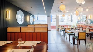 Un restaurant avec des tables rondes, des banquettes et une vue sur les bâtiments environnants.