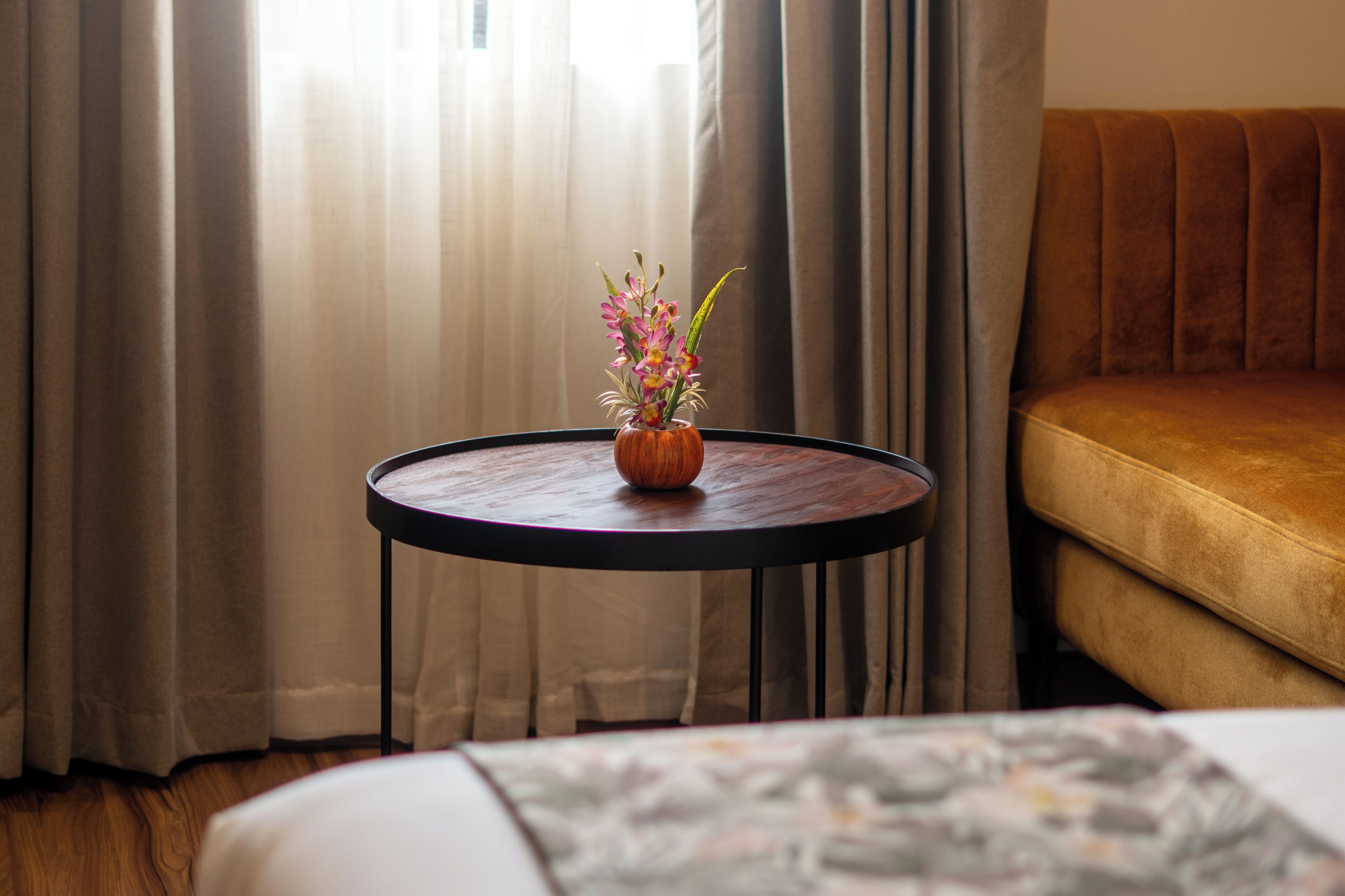 Une table ronde avec un vase de fleurs, un canapé et des rideaux dans une pièce.