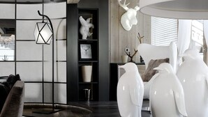 Ein modernes Wohnzimmer mit dunklem Holzboden, einer schwarzen Stehlampe, weißen Dekorationselementen und einer Holzzieldecke.