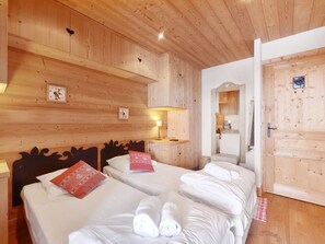 Ein Zimmer mit Holzwänden, zwei Betten, einem Nachttisch, einem an der Wand montierten Regal und einer Tür.