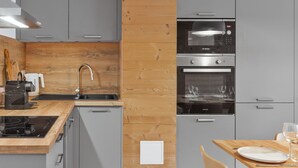 A modern kitchen with grey cabinets, a wooden accent wall, a Bosch oven, and a dining area with a table set for two. - Modern apartment in Monêtier, near the village (Le Monêtier-les-Bains)