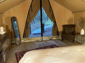 A tent with a bed, a chair, a table, and a view of the outdoors.