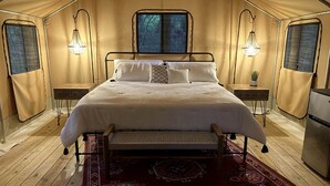 Une pièce aménagée avec une tente, un lit, deux lampes de chevet, une petite table et un réfrigérateur.