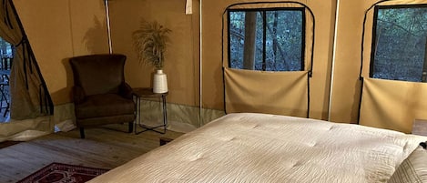 A tented room with a bed, a chair, a small table, and a potted plant.