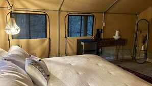 Une pièce aménagée avec une tente, un lit, une petite table, une chaise et une fenêtre.