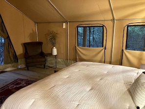 A tented room with a bed, a chair, a small table, and a potted plant.