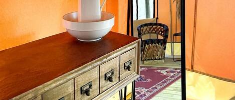 A room with a wooden dresser, a white vase, and a mirror reflecting a tent-like structure.
