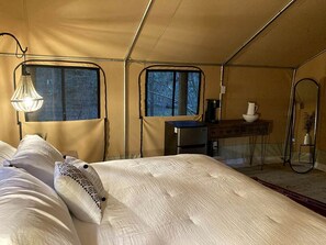 A tented room with a bed, a small table, a chair, and a window.