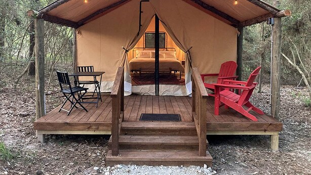 Une tente équipée d’un lit, d’une table, de chaises et d’une terrasse en bois.