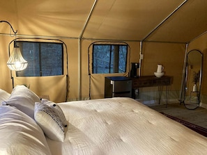 A tented room with a bed, a small table, a chair, and a window.