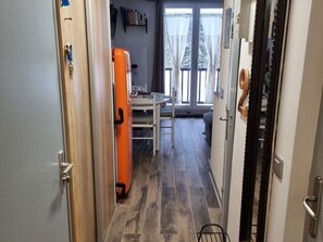 Ein schmaler Flur mit Holzboden, einem weißen Tisch mit Stühlen und einem orangen Kühlschrank.