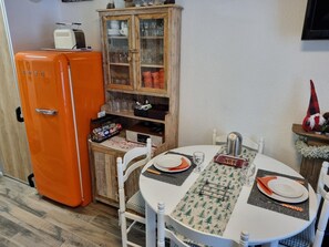 Eine kleine Küche mit einem retro-orangenen Kühlschrank, einem Holzschrank mit Glastüren und einem Esstisch für zwei Personen.