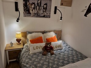 Ein Schlafzimmer mit einem Bett, Kissen, einem Teddybär, einem Nachttisch, einer Lampe und einem Wandbild.