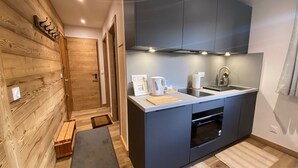 A compact kitchen with dark cabinets, a built-in oven, and a sink. There is a wooden wall on one side and a bench near the entrance. - Studio in Cernix, 4 pers, near slopes, large terrace (Crest-Voland)