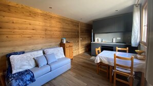 A cozy room with a wooden wall, a sofa, a dining table with chairs, and a kitchenette area. - Studio in Cernix, 4 pers, near slopes, large terrace (Crest-Voland)