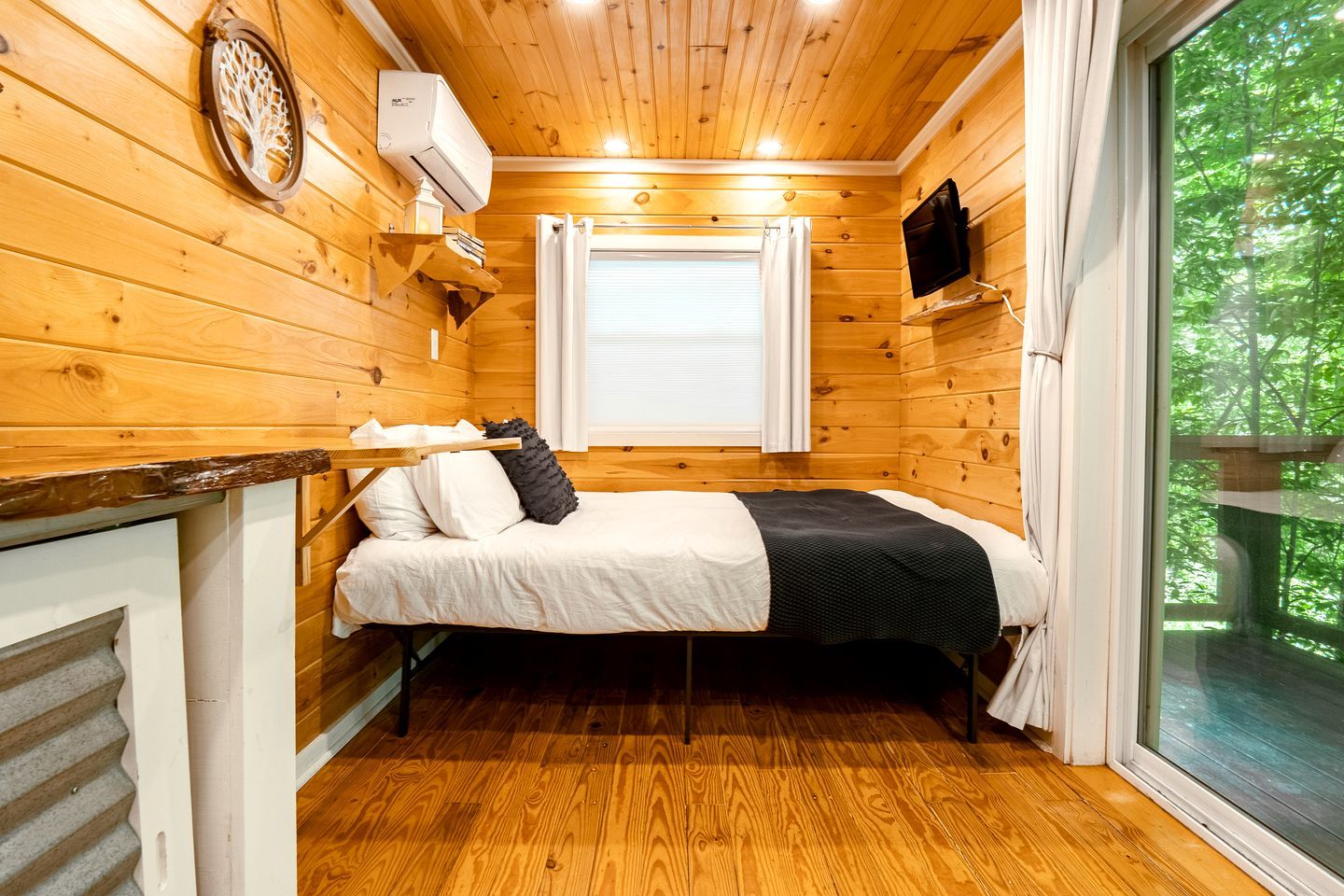 Een houten kamer met een bed, een tv aan de muur en een raam met gordijnen.