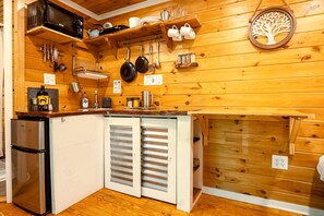 A compact kitchen with wooden walls, a built-in refrigerator, and various kitchen utensils and appliances. - Elevated Getaway: Exclusive Tiny House with Hot Tub and Deck Views in Todd, NC (Todd)