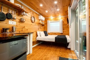 A compact room with a bed, a kitchenette, wooden walls, and a window. - Elevated Getaway: Exclusive Tiny House with Hot Tub and Deck Views in Todd, NC (Todd)