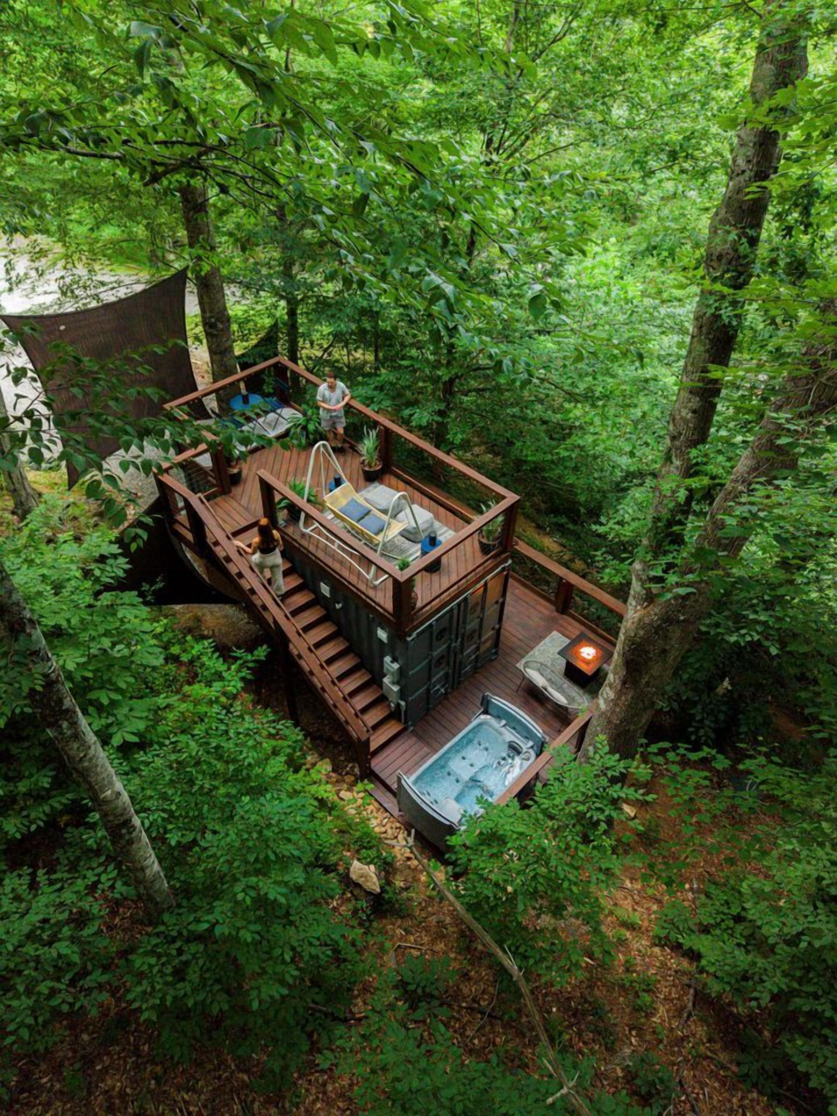 A wooden deck with a hot tub and outdoor seating, surrounded by dense forest.