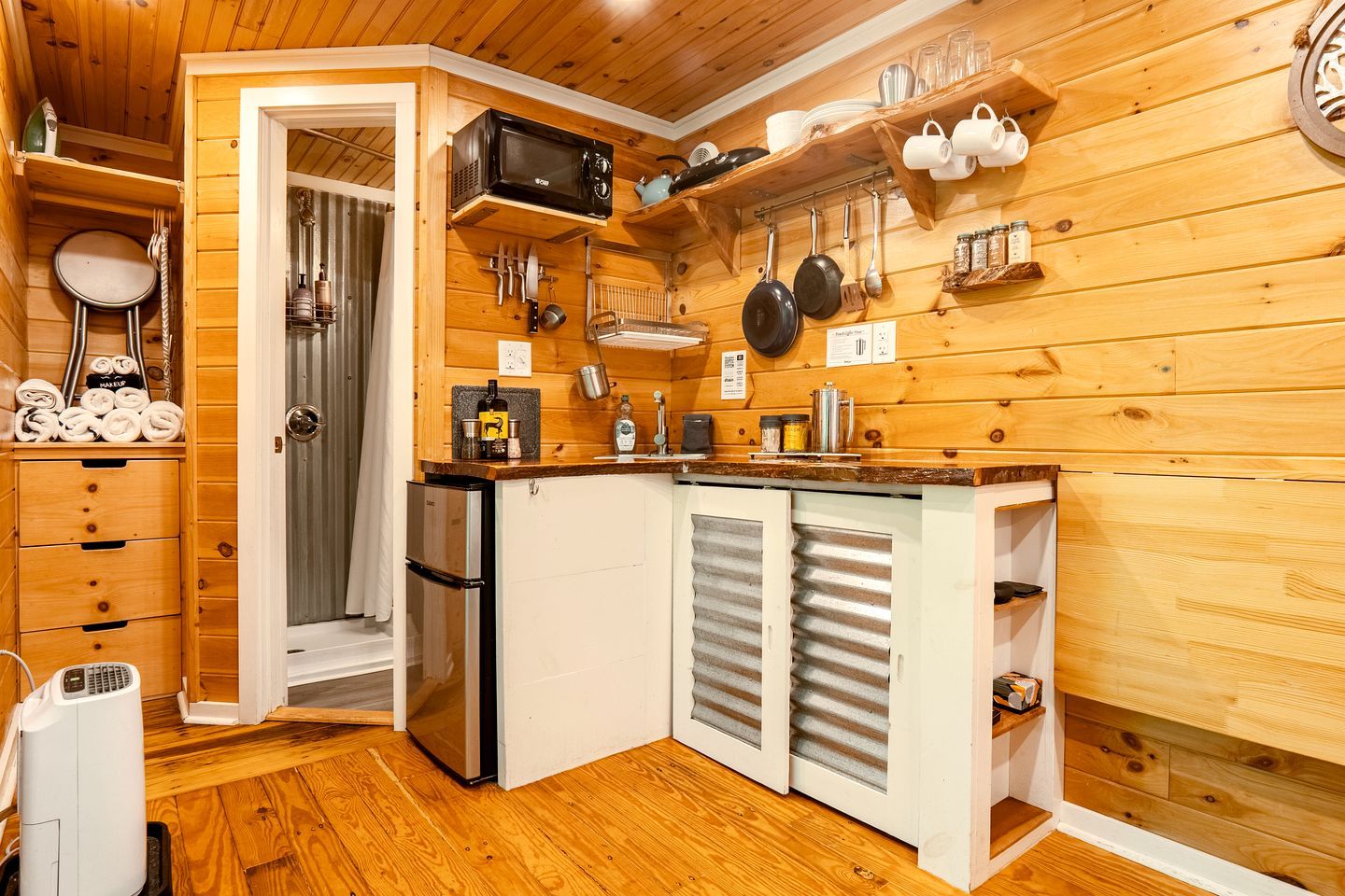 A compact kitchen with wooden walls, a built-in microwave, and various utensils hanging above the counter.