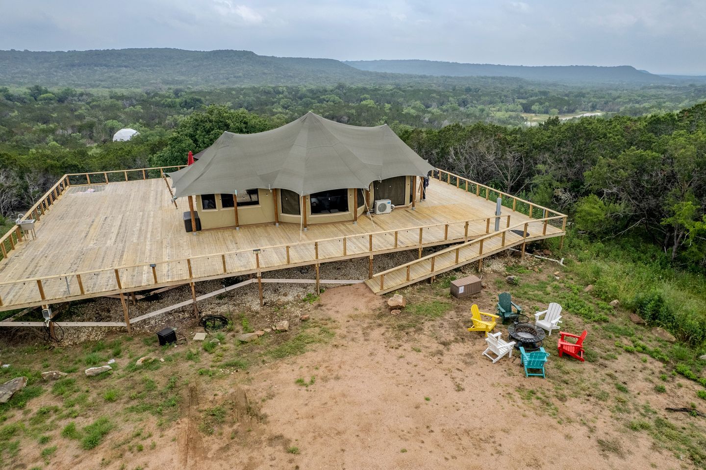 A large, open-air structure with a wooden deck and a covered seating area, surrounded by natural landscape.