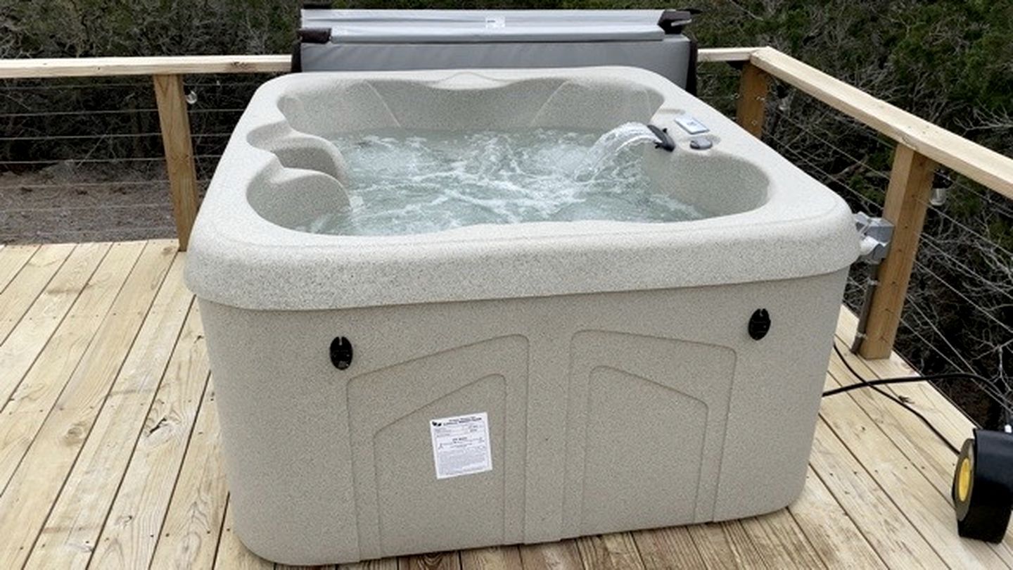 Een hottub op een houten terras, met een houten leuning en een metalen afdekking.
