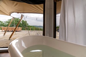 A room with a large bathtub, wooden deck, outdoor seating, and a view of the landscape.