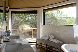 A bathroom with a bathtub, a sink, and a bench with towels. There is a window with a view of trees and a balcony.