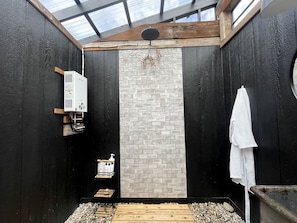 A bathroom with a black and white brick wall, a wooden ceiling, a white towel hanging, and a shower area.