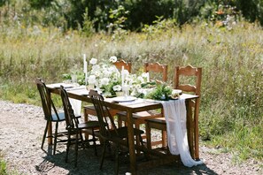 Une table en bois installée à l’extérieur, avec des chaises, et entourée de verdure.