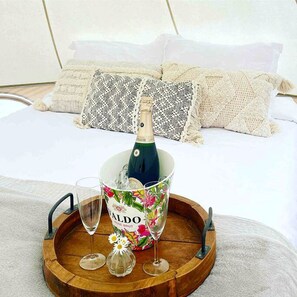 Un lit avec une bouteille de champagne, un seau rempli de fleurs et deux verres sur un plateau en bois.