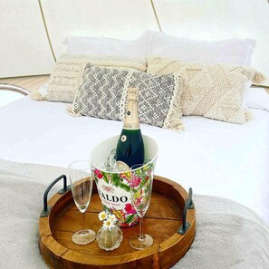 Un lit avec une bouteille de champagne, un seau rempli de fleurs et deux verres sur un plateau en bois.