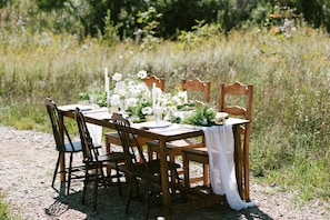 A wooden table set outdoors with chairs, surrounded by natural vegetation.