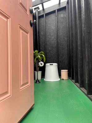A narrow hallway with a green floor, a white trash bin, a potted plant, and a door with a black handle.