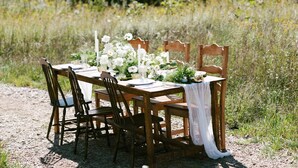 Une table en bois installée à l’extérieur, avec des chaises, et entourée de verdure.