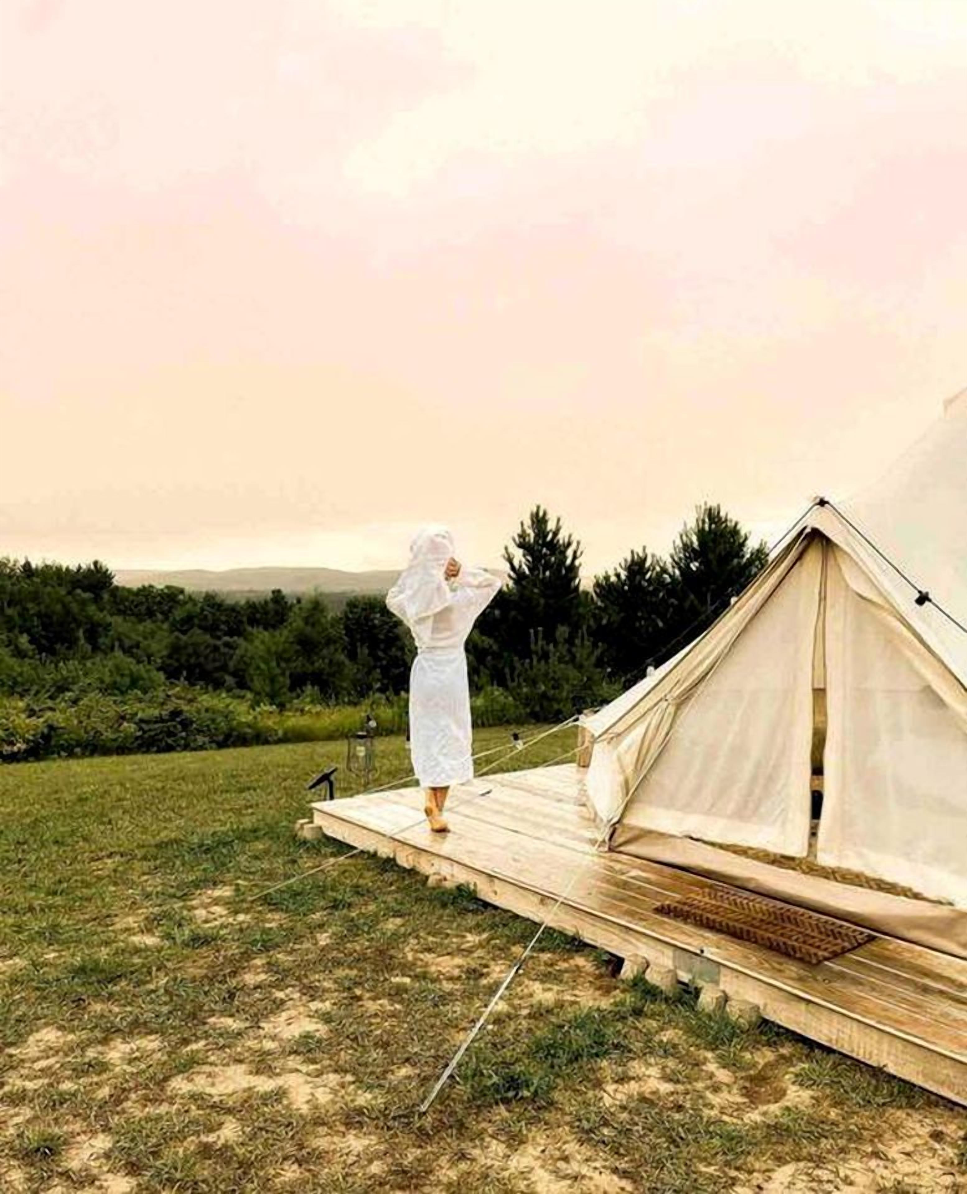 A tent in a grassy field with a person standing nearby.