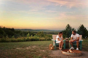 Two people sitting on a bench outdoors with a fire pit in front of them.