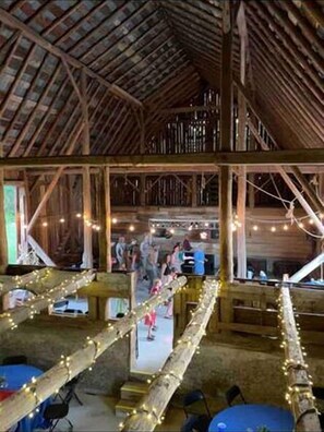 A rustic barn-style interior with wooden beams, tables, and string lights.