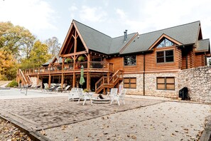 A log cabin with a stone exterior, a balcony with outdoor seating, and a stone wall. - Luxurious Cabin Retreat with Heated Pool and Scenic Creek Views in Wayne Township, IN (Wayne Township)