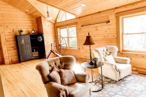 A wooden cabin interior with a large window, a fireplace, a sofa, and a lamp. - Luxurious Cabin Retreat with Heated Pool and Scenic Creek Views in Wayne Township, IN (Wayne Township)