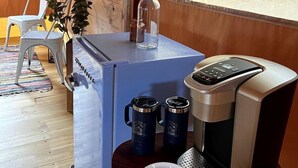 A compact kitchen with a coffee maker, two mugs, a bowl, and a potted plant.