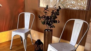 Two white metal chairs, a wooden floor, a wooden wall, a window with a view, and a potted plant.