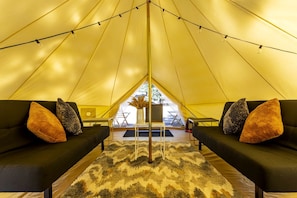 A tent with two black sofas, a patterned rug, and a view of the outdoors.