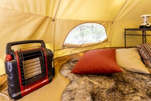 Une tente comprenant un espace de couchage, un chauffage portable et une fenêtre donnant sur les arbres.